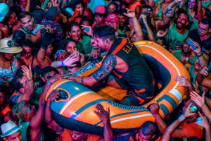 Foto do cantor Felipe Pezzoni cantando em cima de um bote inflável carregado pelos foliões do bloco EVA