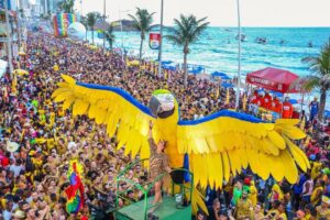 Foto da cantora Claudia Leitte vestida de onça em frente a uma grande Arara amarela ornamentada no seu trio do Carnaval de Salvador